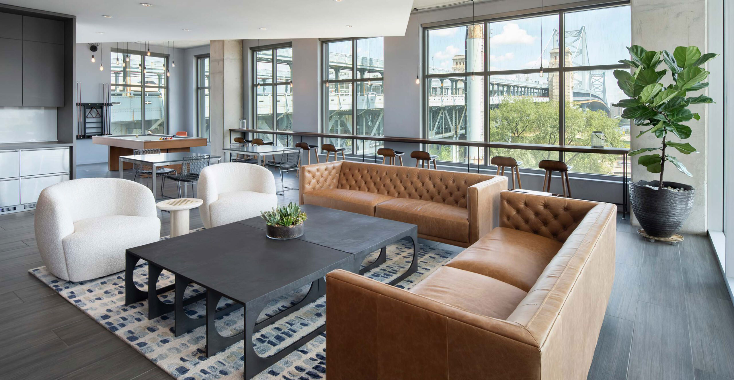 Modern lounge with large windows, brown leather sofas, white chairs, and a black coffee table on a patterned rug. Bright, airy atmosphere.