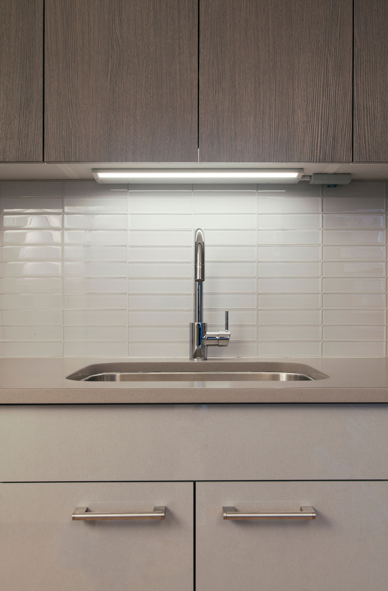 Modern kitchen with sleek wood cabinets and a white tile backsplash. A stainless steel faucet and under-cabinet lighting add a clean, minimalist feel.