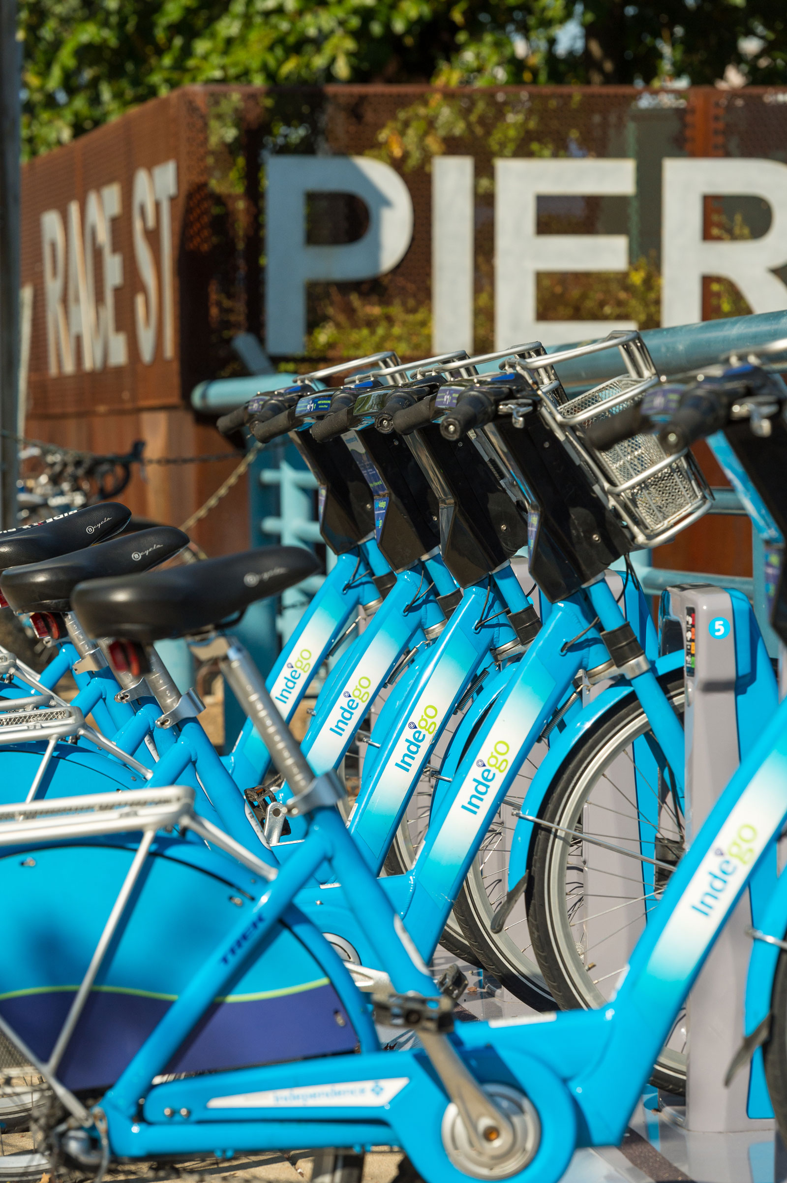 Bright blue Indego rental bikes are lined up at Race Street Pier. The atmosphere is vibrant, urban, and inviting, emphasizing outdoor activity.